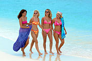 Four women in bikinis walk on beach